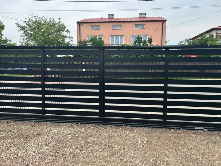Czarna brama przesuwna z poziomych profili przy posesji